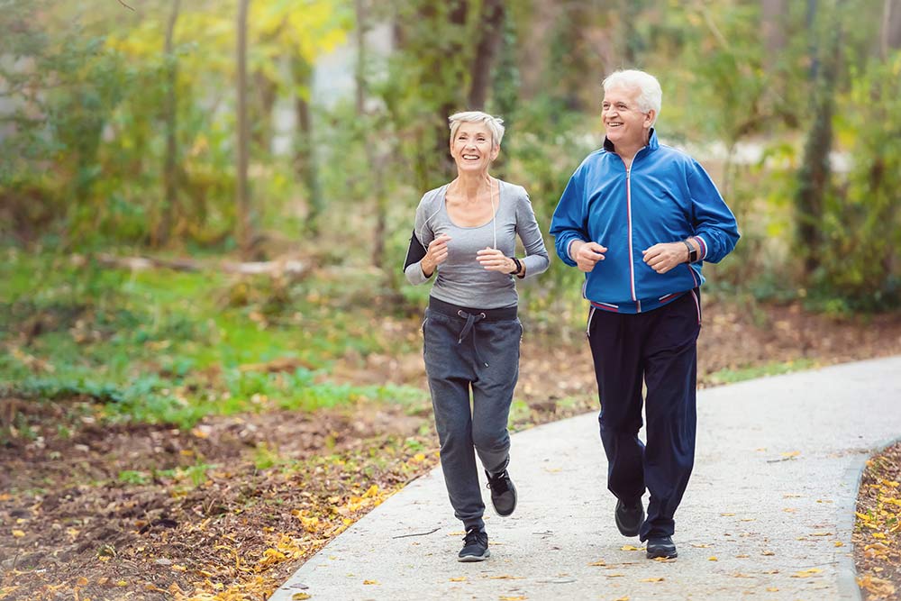 Smiling senior active couple jogging together in the park