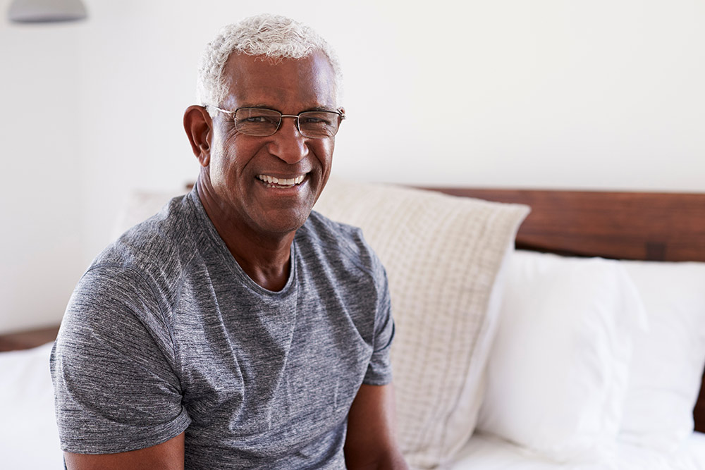 Portrait Of Smiling Senior Man Sitting On Side Of Bed