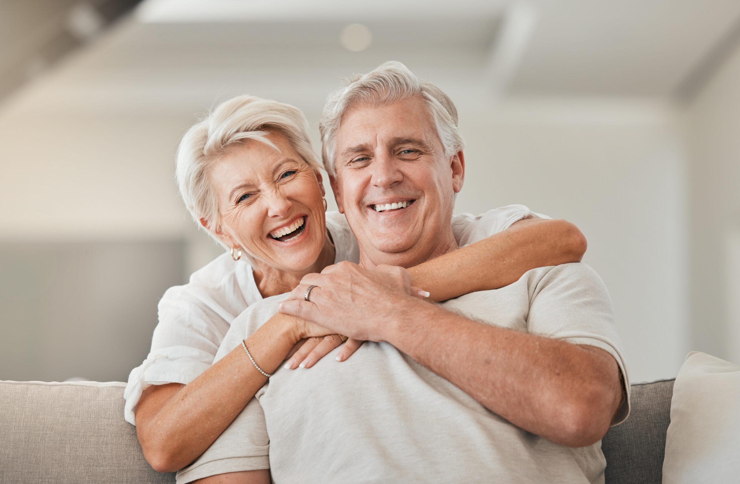 Happy senior couple, portrait and hug on living room sofa for embrace, relationship or love at home. Mature woman hugging man with smile in happiness for care, support or trust together in house.